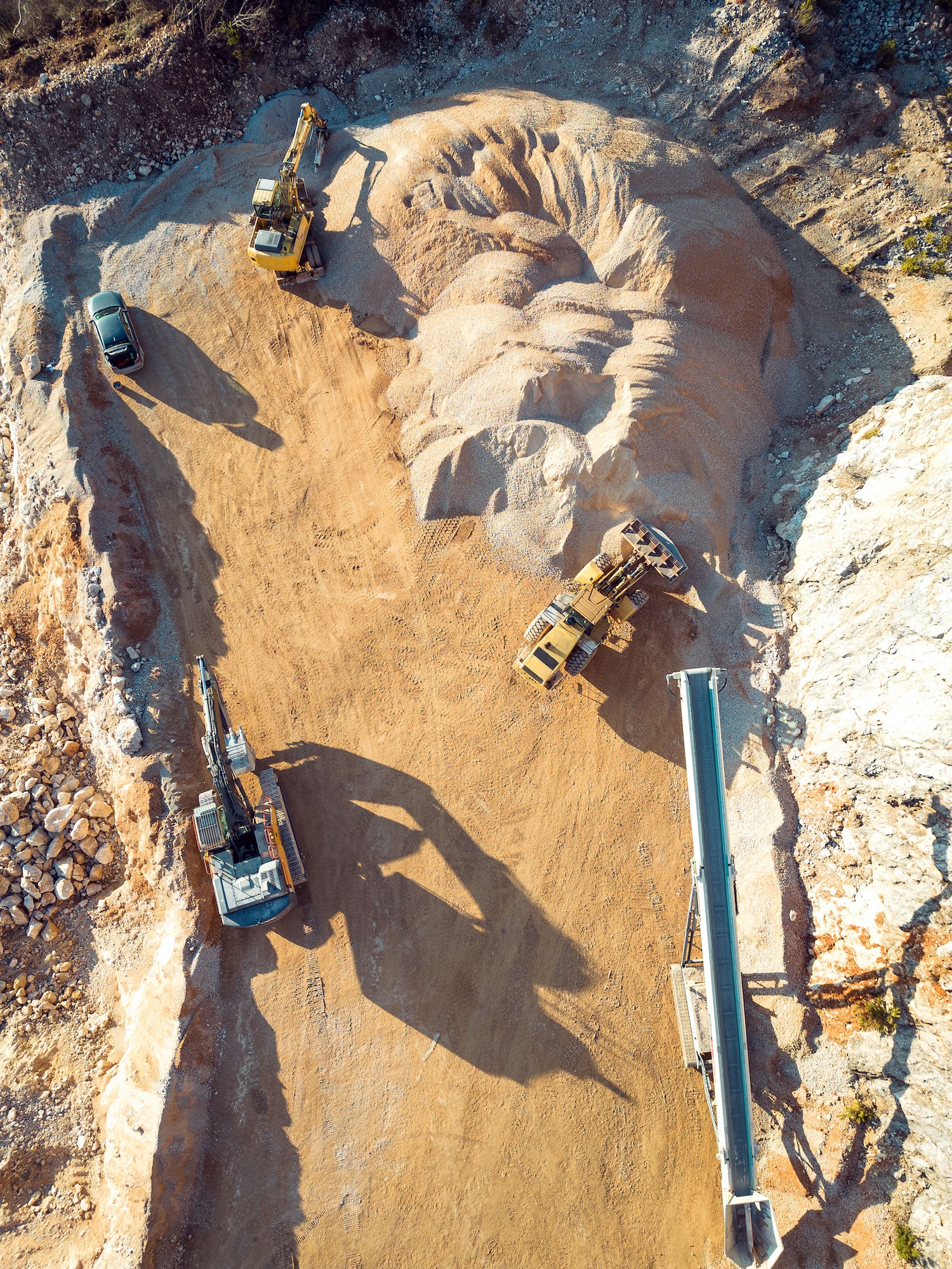 Vertical photo of yellow heavy machinery, excavators working on dusty quarry grounds